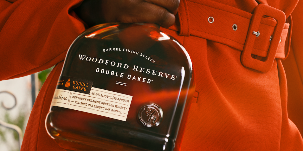 Close up of a woman's hand holding a bottle of Woodford Reserve Double Oaked against a red coat.